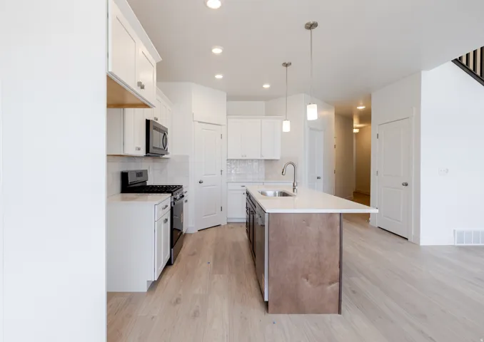 Dual tone kitchen featuring stainless steel appliances, dual tone cabinetry, a kitchen island with sink, light wood-style floors, and light stone countertops