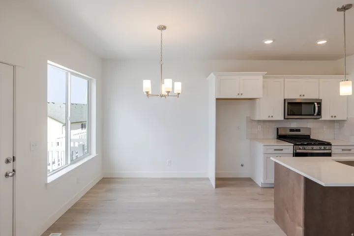 Kitchen with stainless steel appliances, light wood-style flooring, tasteful backsplash, a chandelier, and light stone countertops
