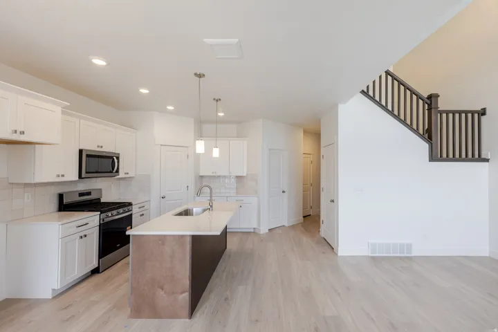 Kitchen with stainless steel appliances, a kitchen island with sink, light wood finished floors, tasteful backsplash, and light stone countertops
