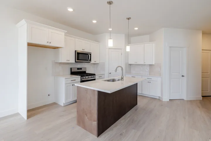 Kitchen featuring stainless steel appliances, a kitchen island with sink, light wood-type flooring, light stone countertops, and two tone color scheme