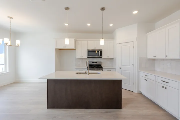 Dual tone kitchen with light wood-style flooring, a center island with sink, stainless steel appliances, light stone counters, and a chandelier