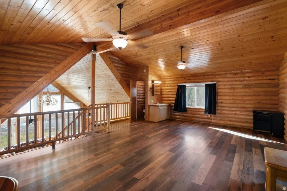 Unfurnished living room featuring hardwood / wood-style flooring, rustic walls, a chandelier, ceiling fan, and wood ceiling