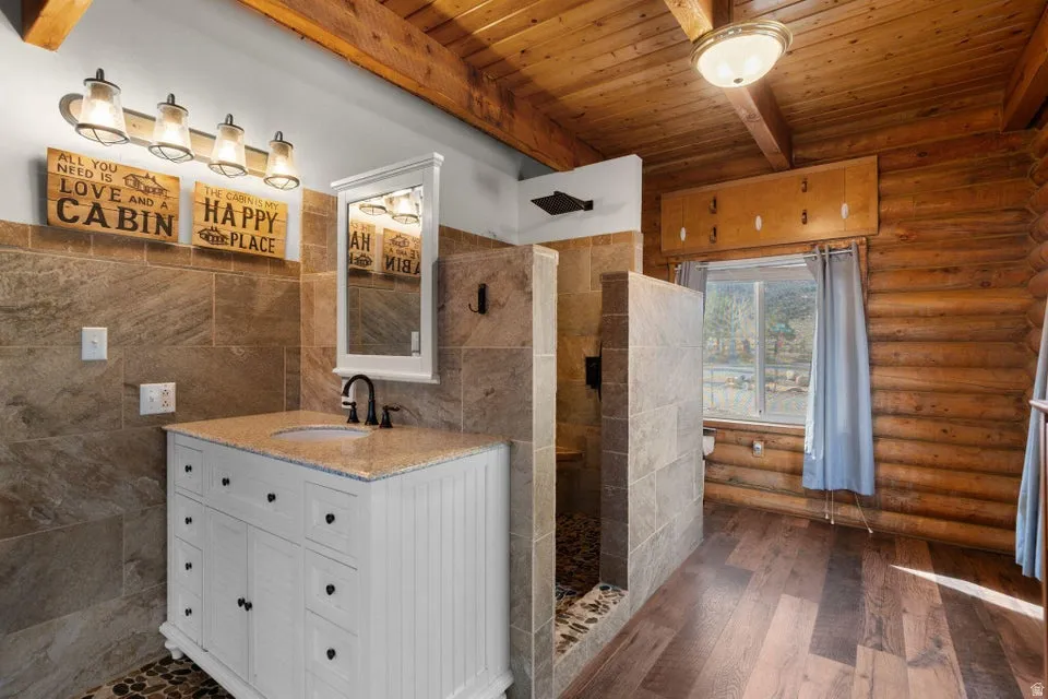 Bathroom with vanity, a wood ceiling with exposed beams, walk in shower, dark wood-style floors, and tile walls