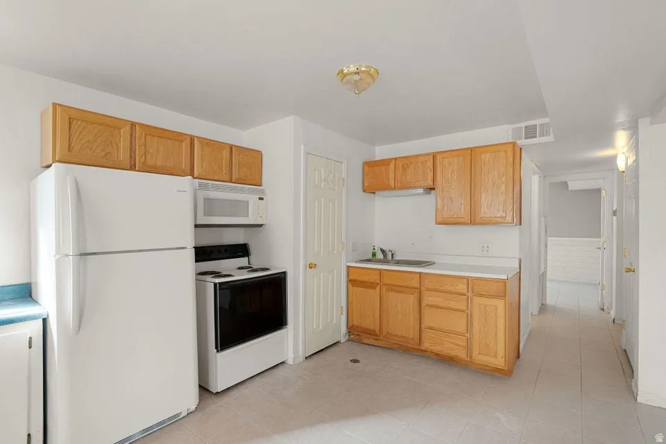Kitchen with white appliances, light countertops, light tile patterned floors, and light brown cabinets