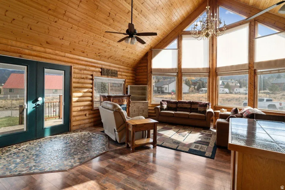 Living area featuring high vaulted ceiling, wooden ceiling, dark wood-type flooring, log walls, and a chandelier