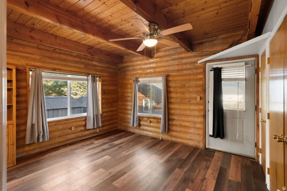 Unfurnished room with wood-type flooring, a ceiling fan, and a wooden ceiling with exposed beams