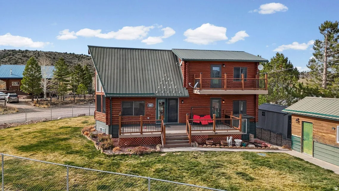 Back of property with a fenced backyard, a metal roof, a balcony, a shed, and a wooden deck