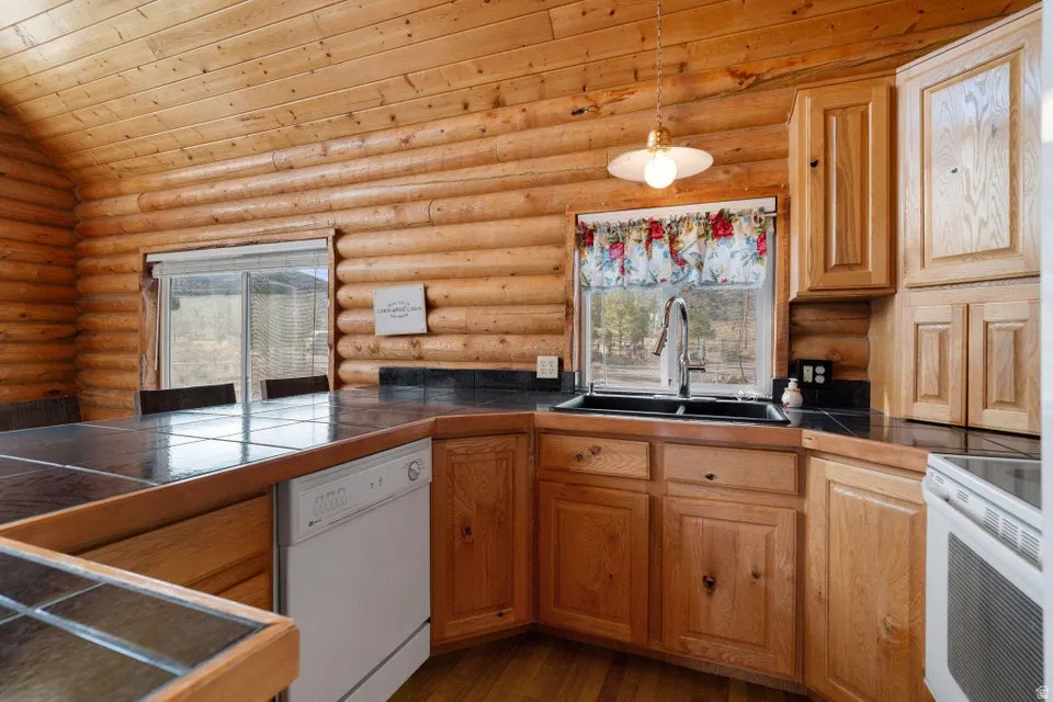 Kitchen with white appliances, dark wood-style flooring, decorative light fixtures, brown cabinetry, and rustic walls