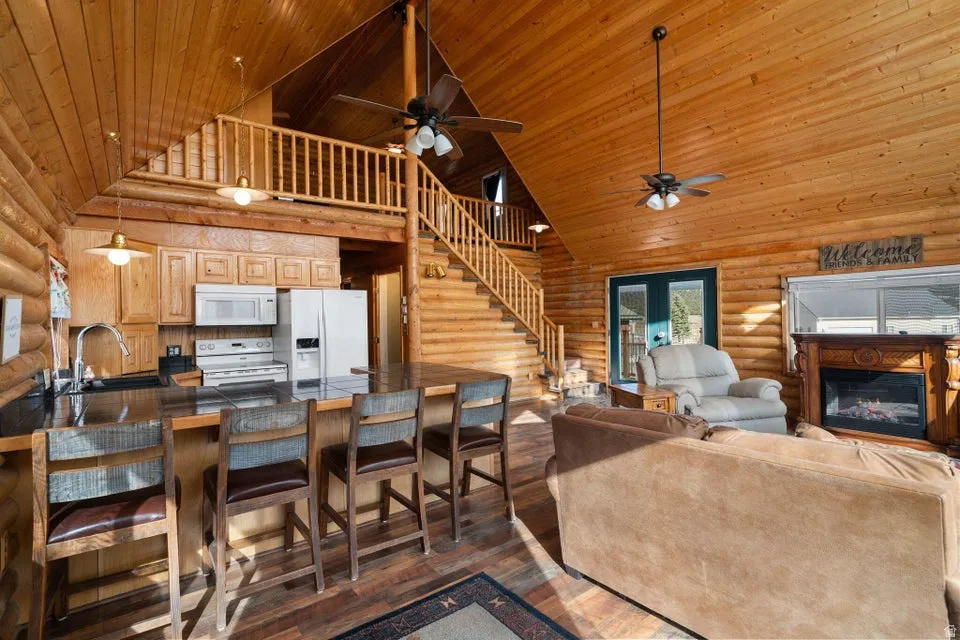 Living area with log walls, high vaulted ceiling, a glass covered fireplace, dark wood finished floors, and wood ceiling