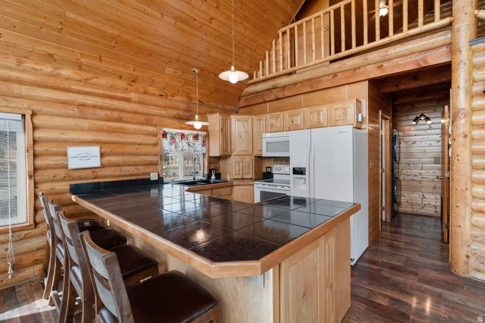 Kitchen featuring rustic walls, a breakfast bar, pendant lighting, high vaulted ceiling, and light brown cabinetry