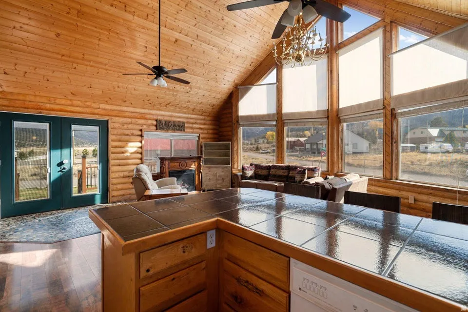 Kitchen with high vaulted ceiling, log walls, wooden ceiling, dark countertops, and a glass covered fireplace