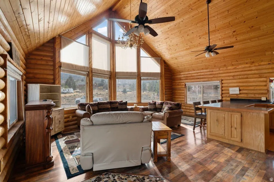 Living area featuring high vaulted ceiling, rustic walls, plenty of natural light, dark wood finished floors, and wooden ceiling