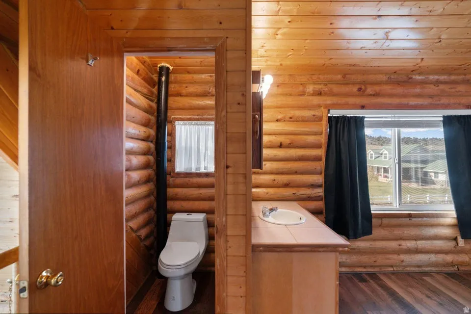 Half bath with vanity, plenty of natural light, log walls, and wood finished floors