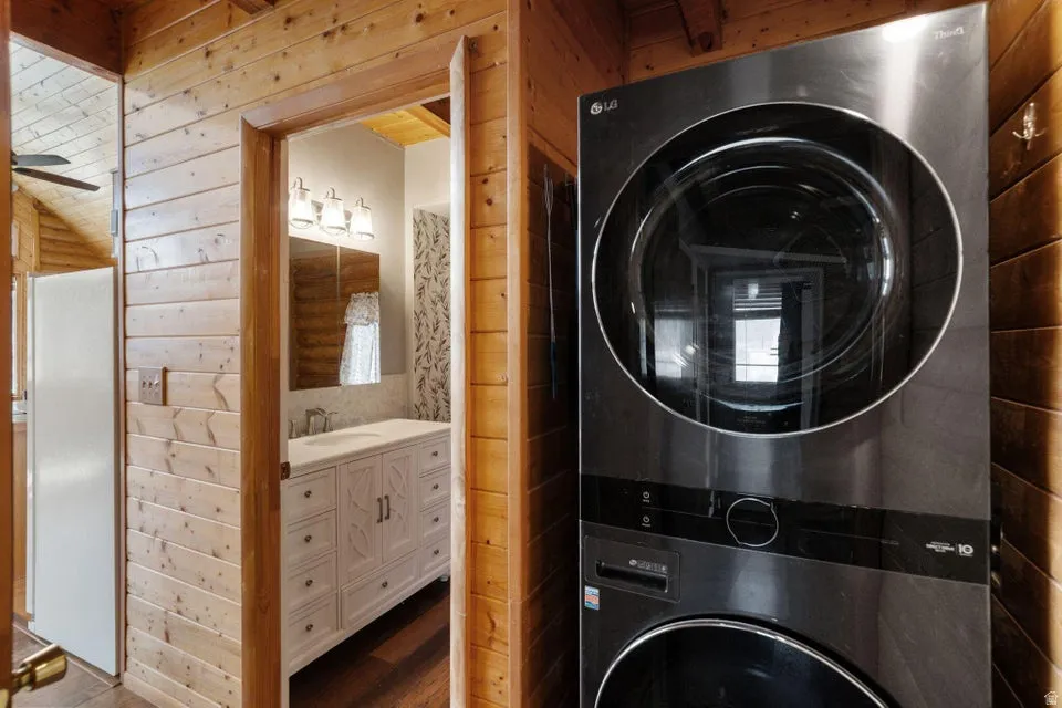 Laundry area featuring wood walls, stacked washer / dryer, wood finished floors, and a ceiling fan