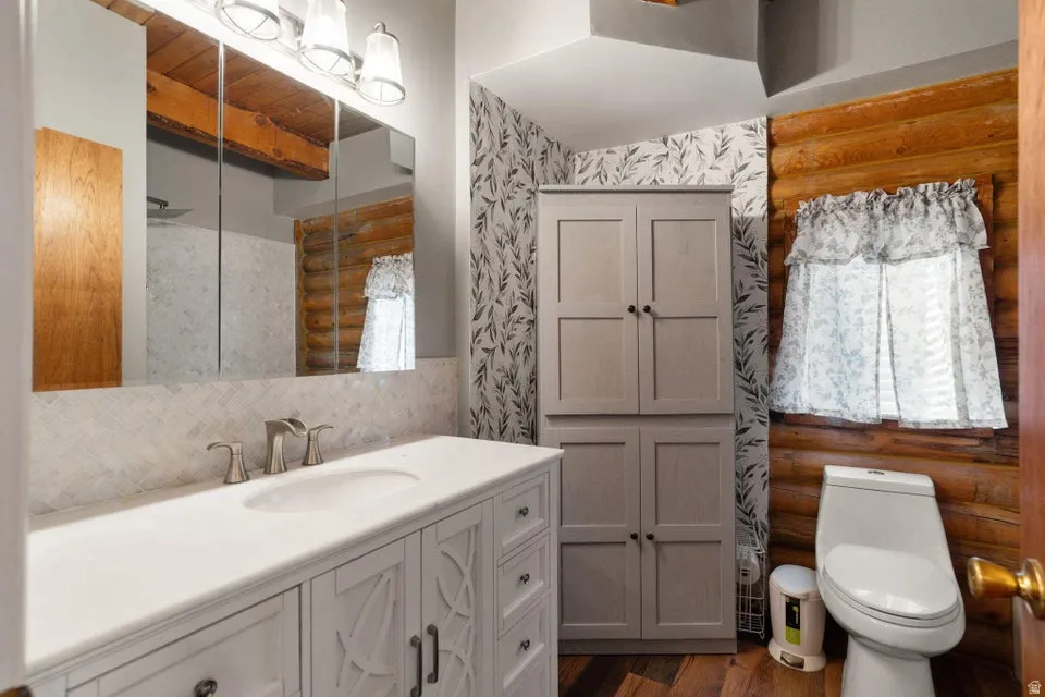 Full bath featuring log walls, vanity, dark wood-type flooring, and beam ceiling