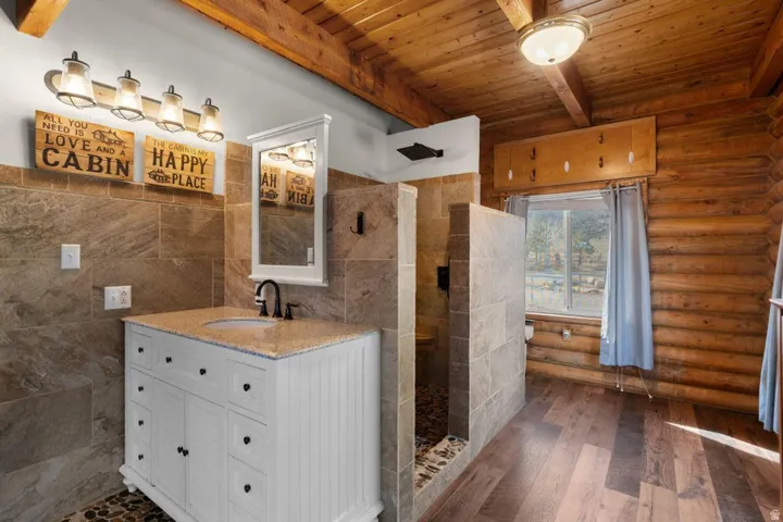 Bathroom with vanity, a wood ceiling with exposed beams, walk in shower, dark wood-style floors, and tile walls
