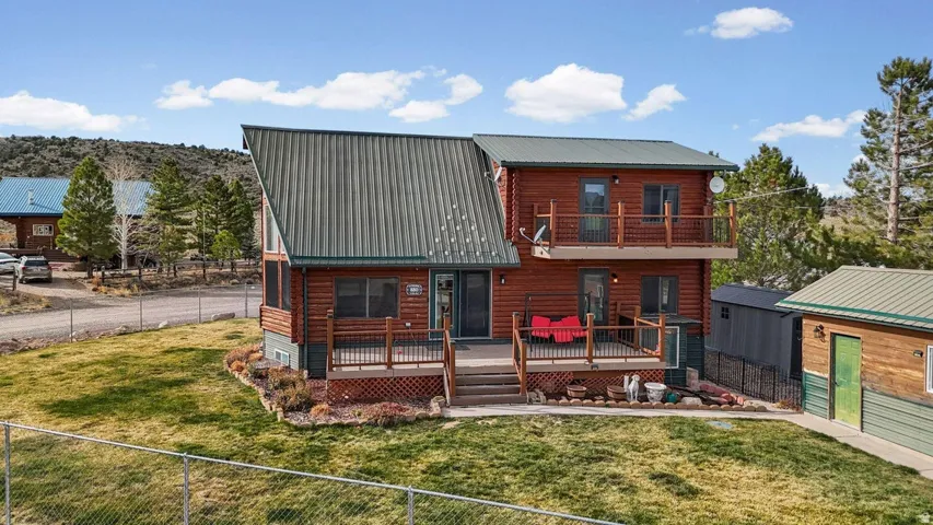 Back of property with a fenced backyard, a metal roof, a balcony, a shed, and a wooden deck