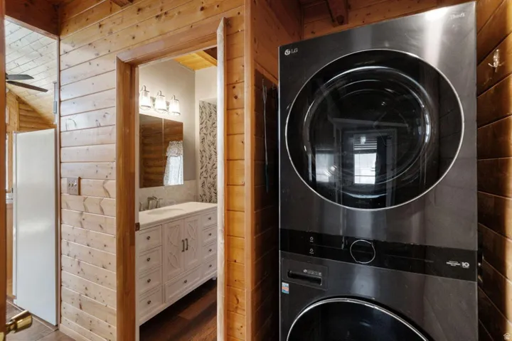Laundry area featuring wood walls, stacked washer / dryer, wood finished floors, and a ceiling fan