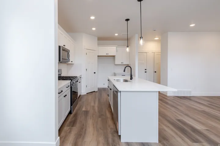 Kitchen featuring stainless steel appliances, a kitchen island with sink, white cabinetry, and dark wood-style floors