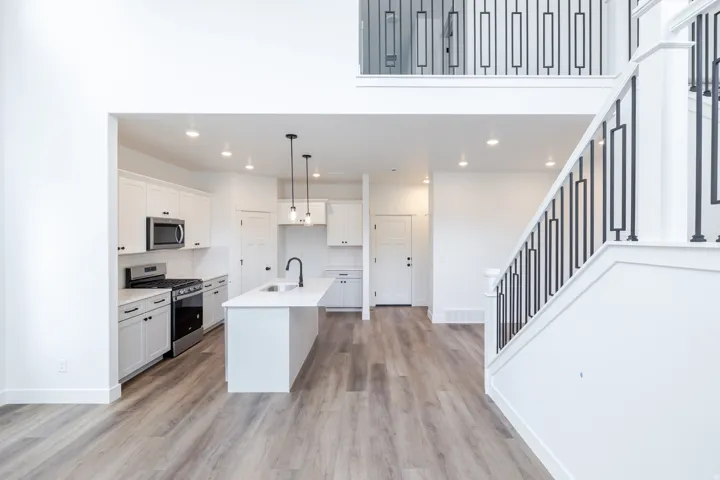 Kitchen featuring stainless steel appliances, white cabinets, light wood-style flooring, a kitchen island with sink, and decorative light fixtures