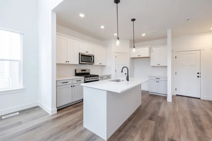 Kitchen with white cabinetry, stainless steel appliances, a kitchen island with sink, and light wood-type flooring
