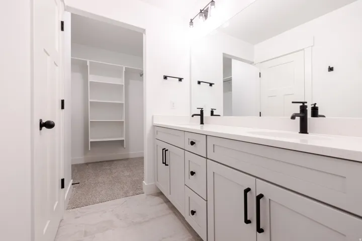 Full bathroom featuring double vanity, a spacious closet, and light marble finish flooring