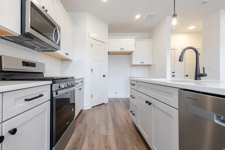 Kitchen with stainless steel appliances, white cabinets, backsplash, light wood-style flooring, and hanging light fixtures