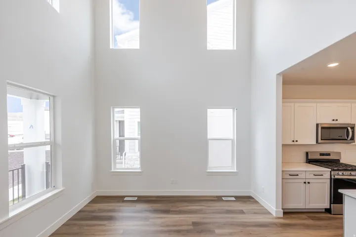 Kitchen with stainless steel appliances, wood finished floors, white cabinetry, backsplash, and a high ceiling