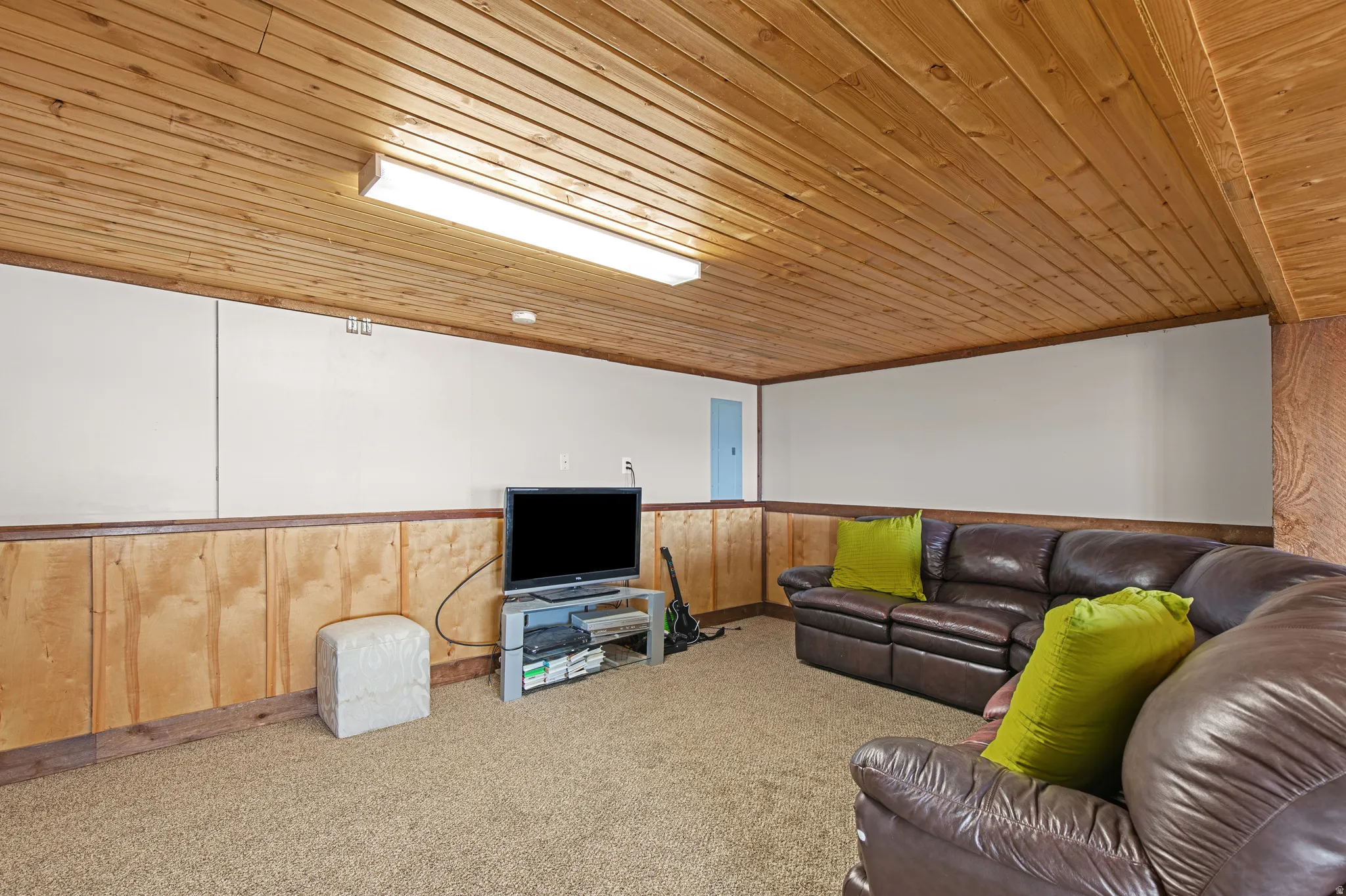 Living area with carpet flooring, wooden walls, wood ceiling, and wainscoting