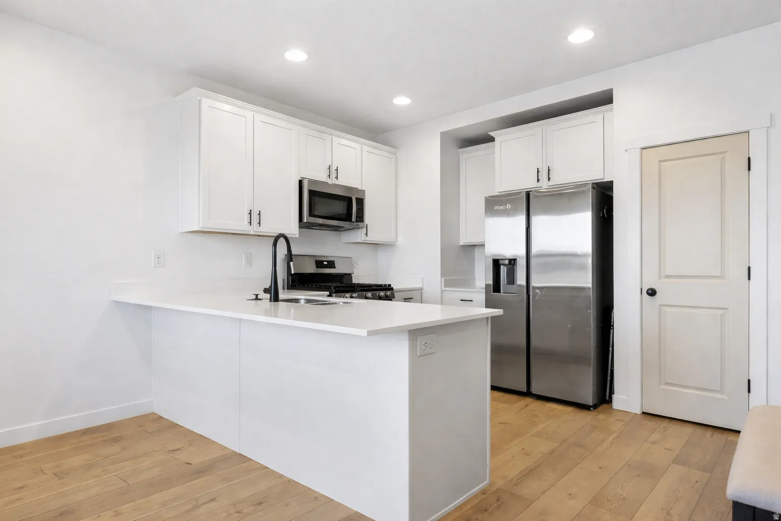 Kitchen with stainless steel appliances, a peninsula, white cabinetry, light wood finished floors, and recessed lighting