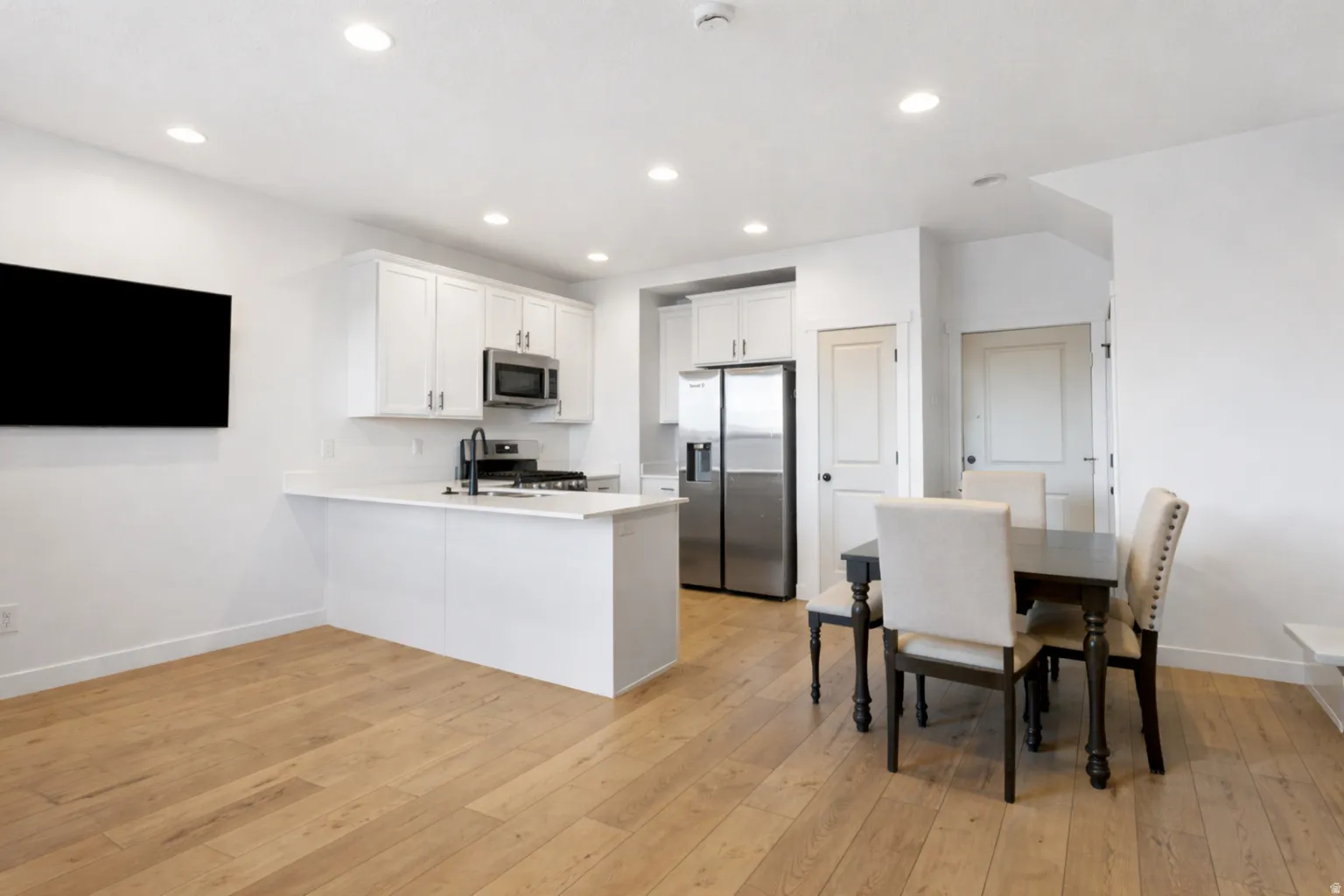 Kitchen featuring white cabinets, stainless steel appliances, a peninsula, light wood-type flooring, and recessed lighting