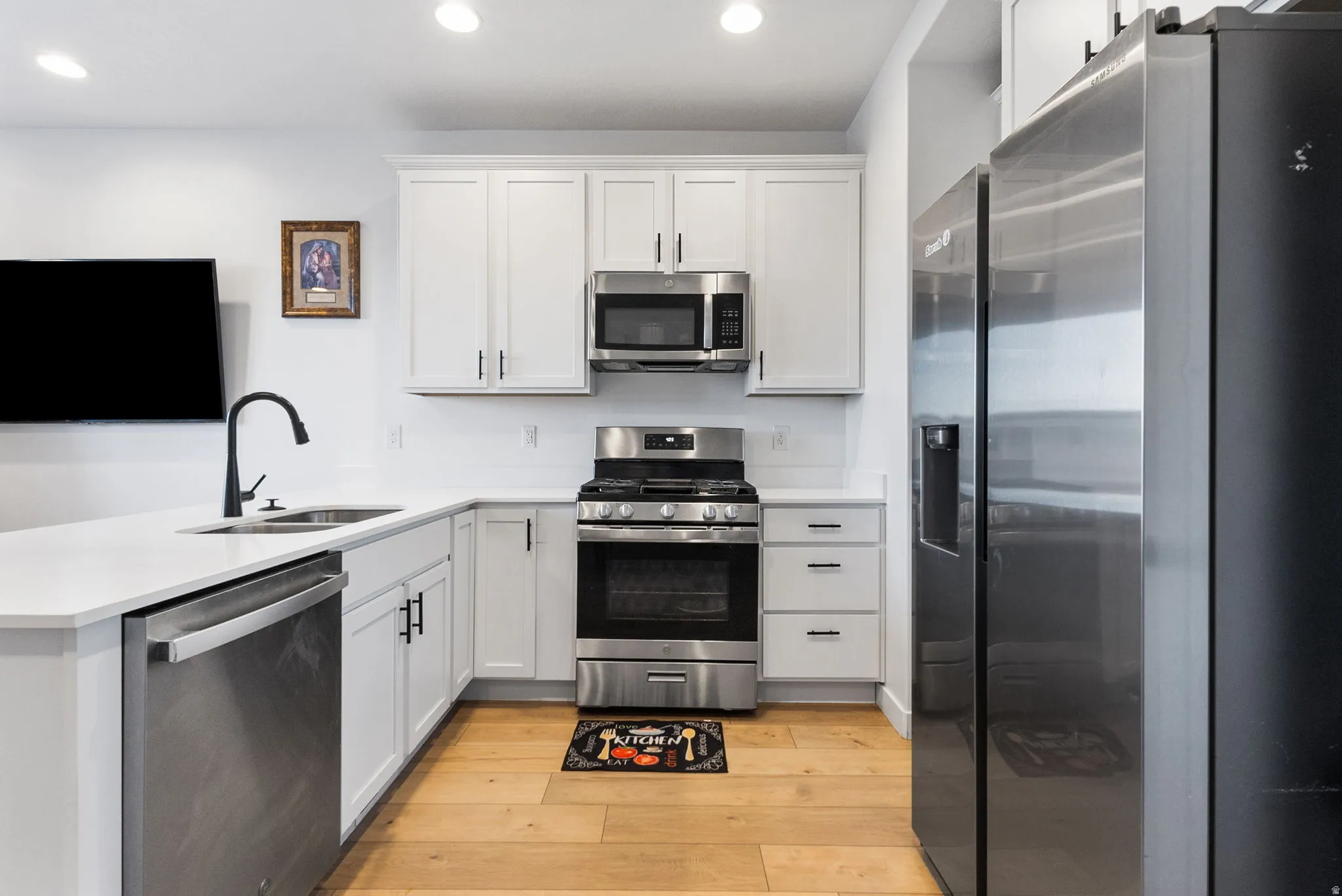 Kitchen with stainless steel appliances, white cabinets, a peninsula, light wood finished floors, and recessed lighting