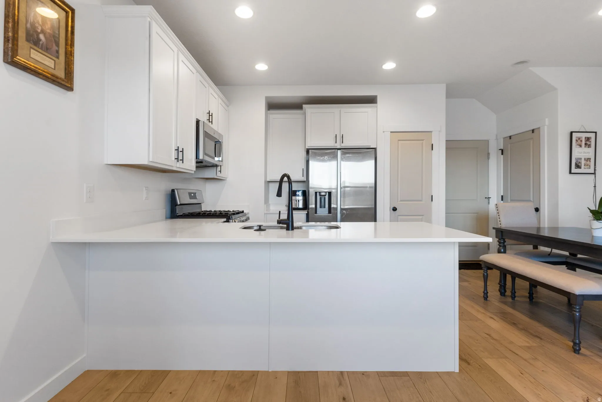Kitchen featuring white cabinets, a peninsula, recessed lighting, stainless steel appliances, and light wood-style flooring