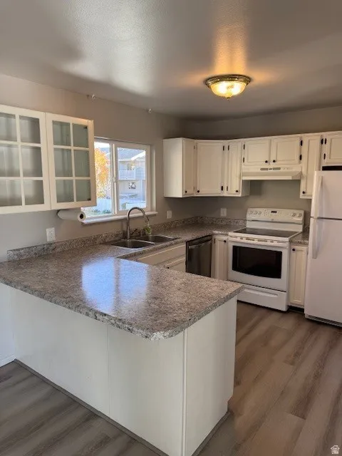 Kitchen featuring white appliances, a peninsula, dark wood-style floors, glass insert cabinets, and a textured ceiling