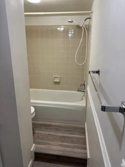 Full bathroom with dark wood-type flooring,  shower combination, and a textured ceiling
