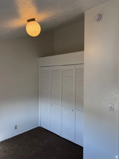 Bedroom featuring a textured ceiling, dark carpet, and a closet