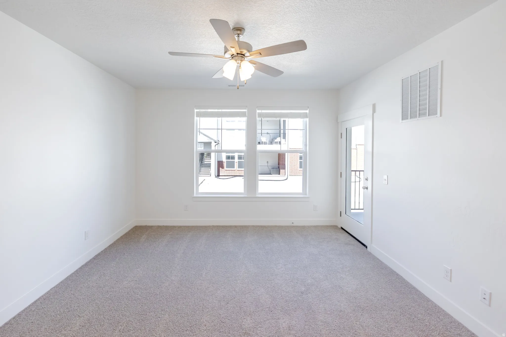 Empty room featuring light carpet, a ceiling fan, and a textured ceiling