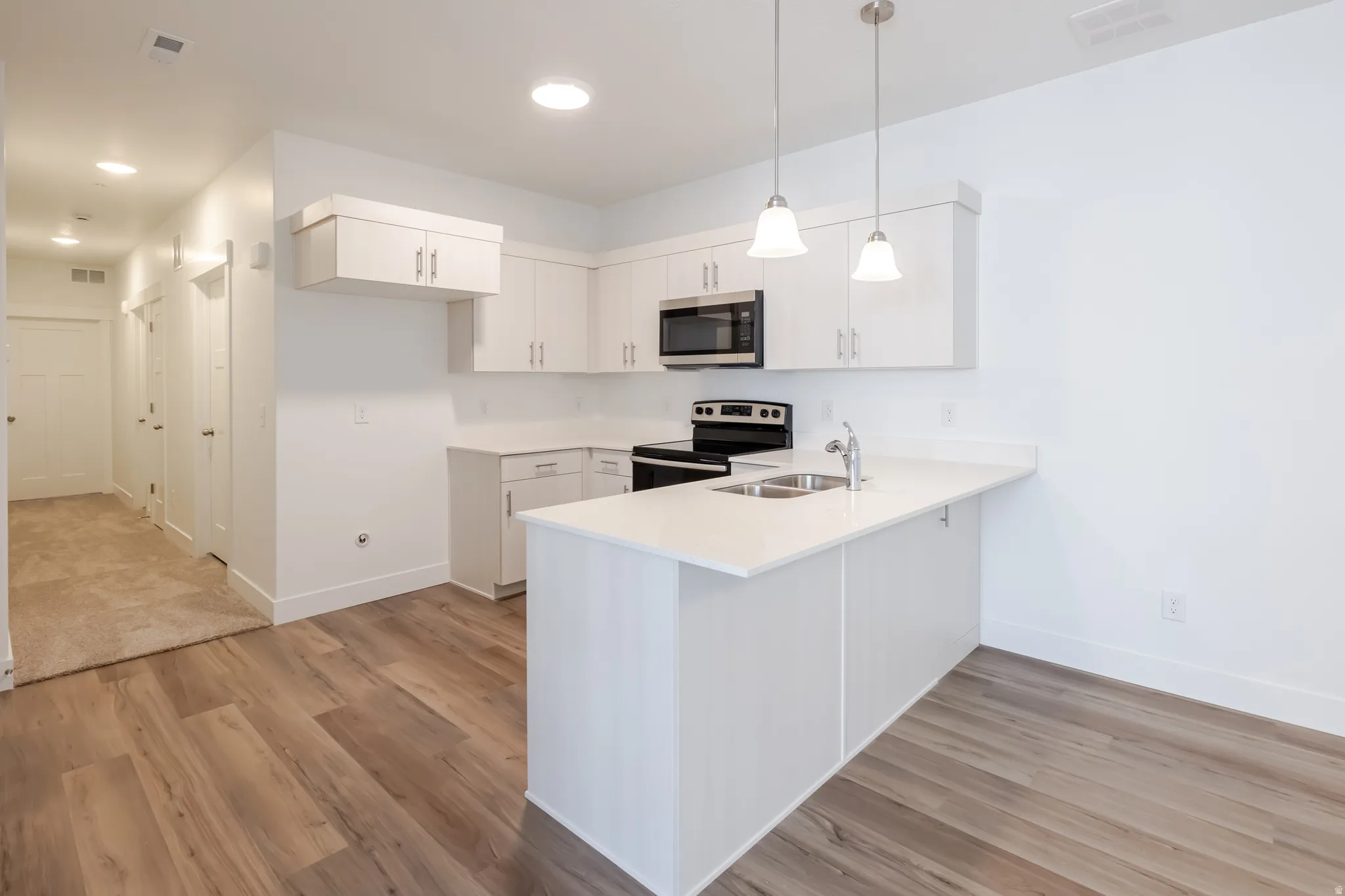 Kitchen with stainless steel appliances, a peninsula, white cabinets, and light wood-type flooring