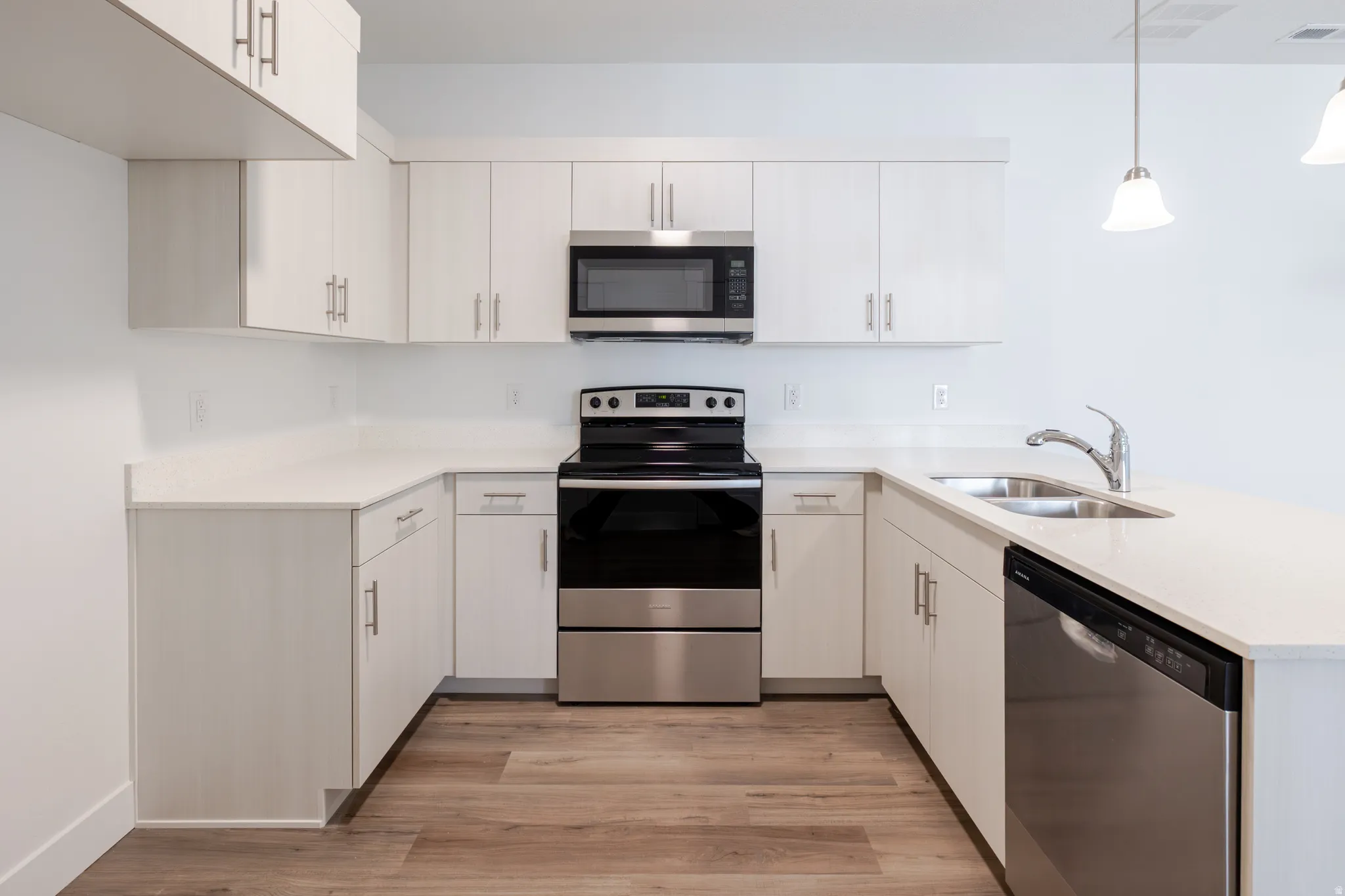 Kitchen featuring stainless steel appliances, a peninsula, light wood-type flooring, pendant lighting, and light stone countertops