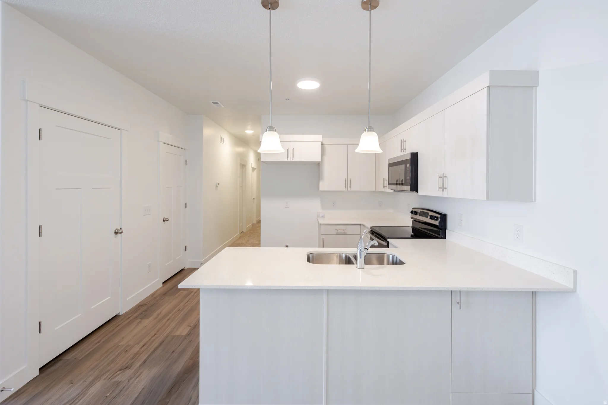 Kitchen with a peninsula, stainless steel appliances, pendant lighting, dark wood finished floors, and white cabinets