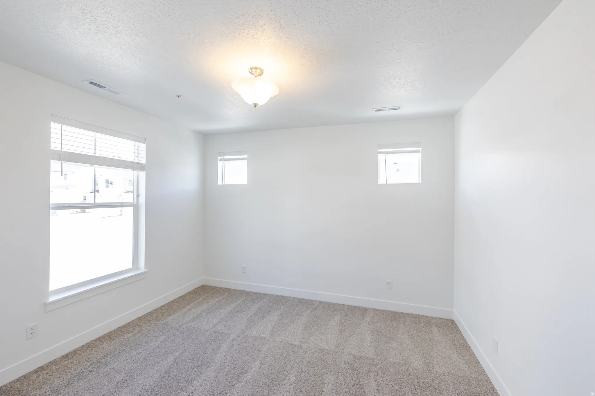 Empty room featuring light carpet, plenty of natural light, and a textured ceiling