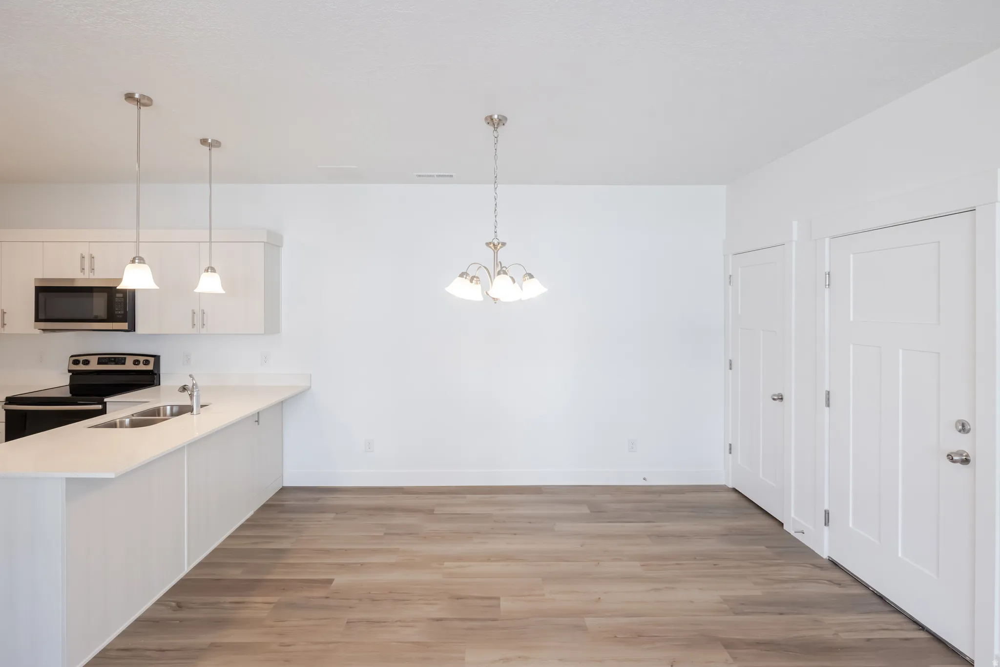 Kitchen with a peninsula, stainless steel appliances, hanging lights, light wood-style floors, and white cabinets