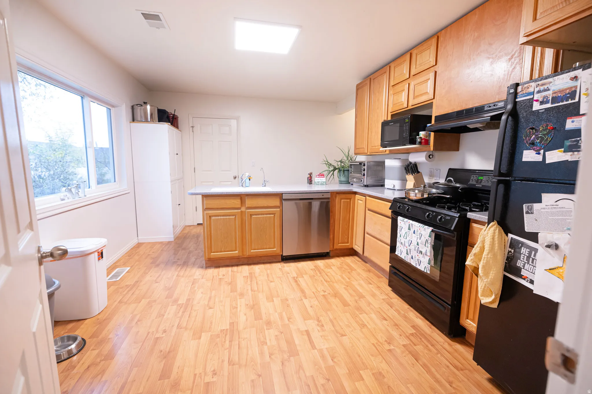 Kitchen featuring a peninsula, black appliances, light countertops, light wood finished floors, and under cabinet range hood