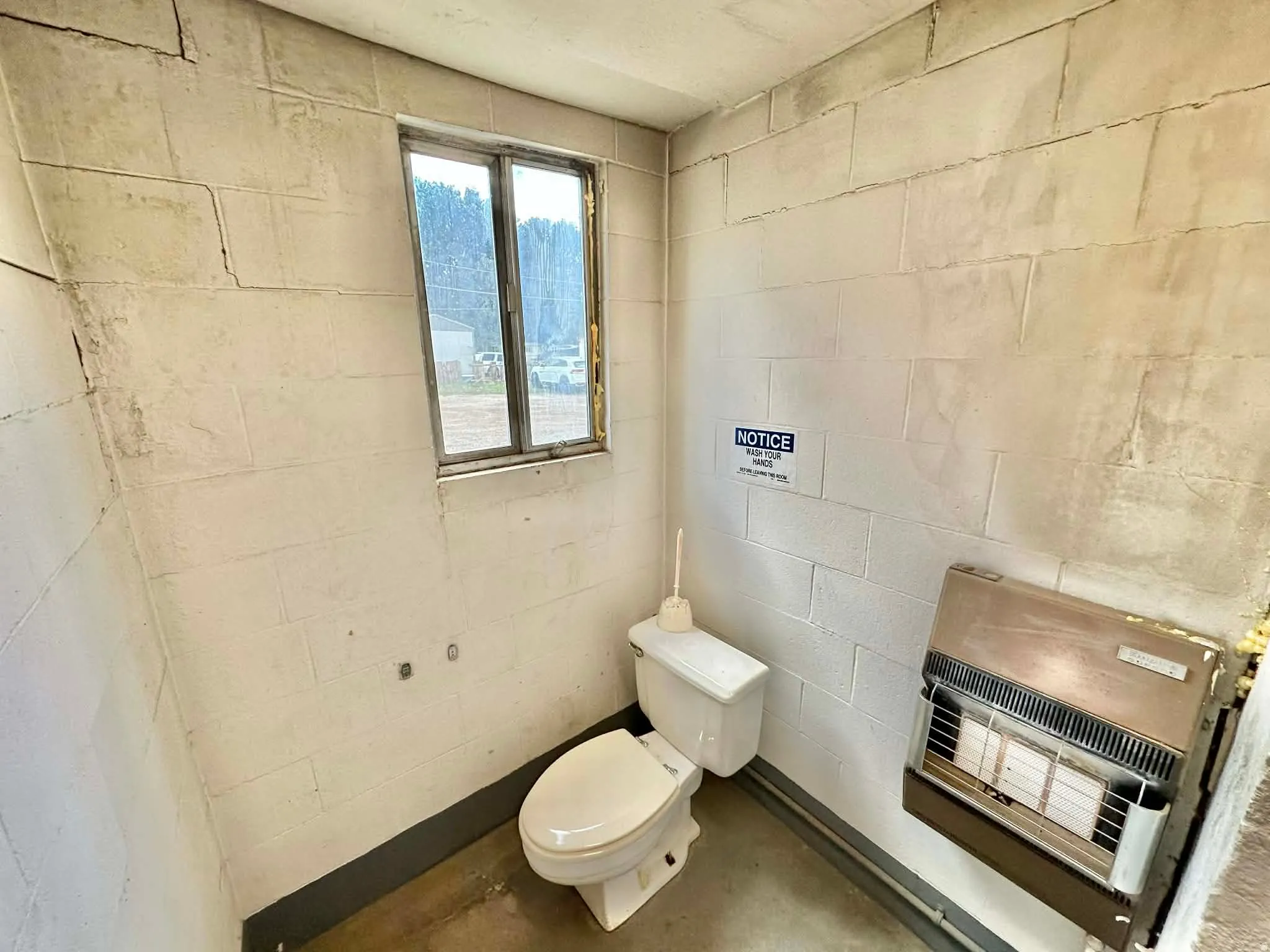 Bathroom with concrete block wall, heating unit, and concrete flooring