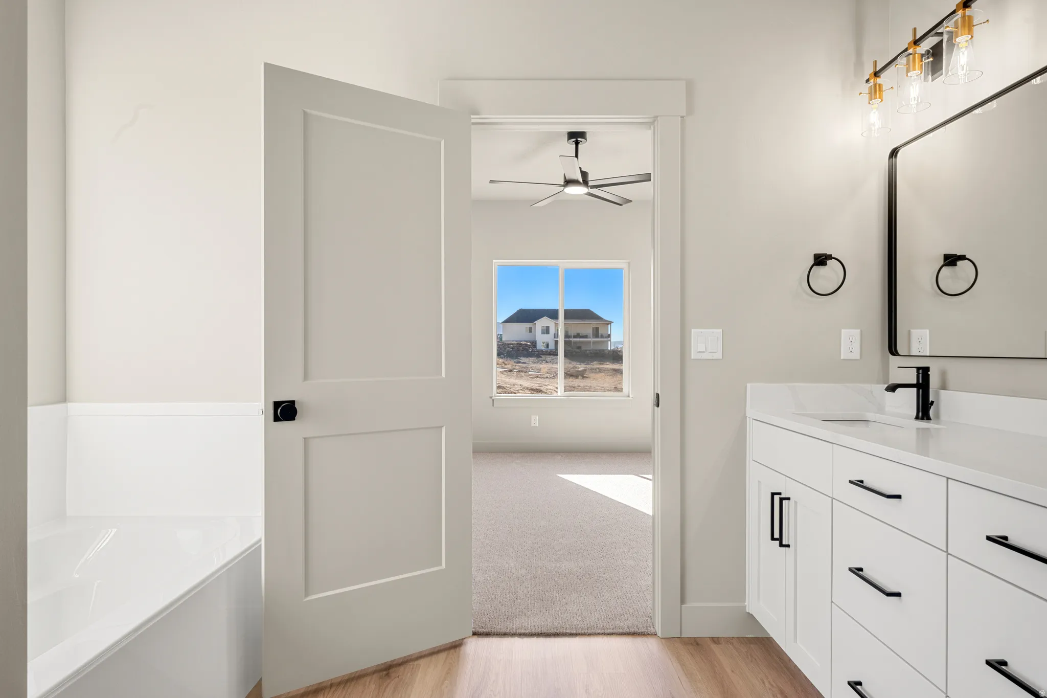 Bathroom with light wood-style floors, vanity, a garden tub, ceiling fan, and light colored carpet