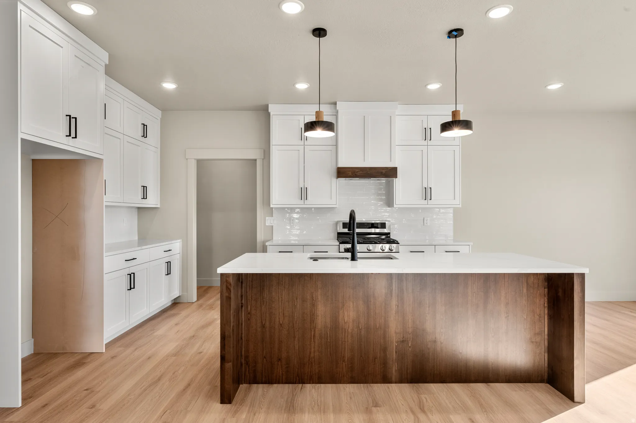 Kitchen with hanging light fixtures, recessed lighting, white cabinetry, a center island with sink, and light stone counters