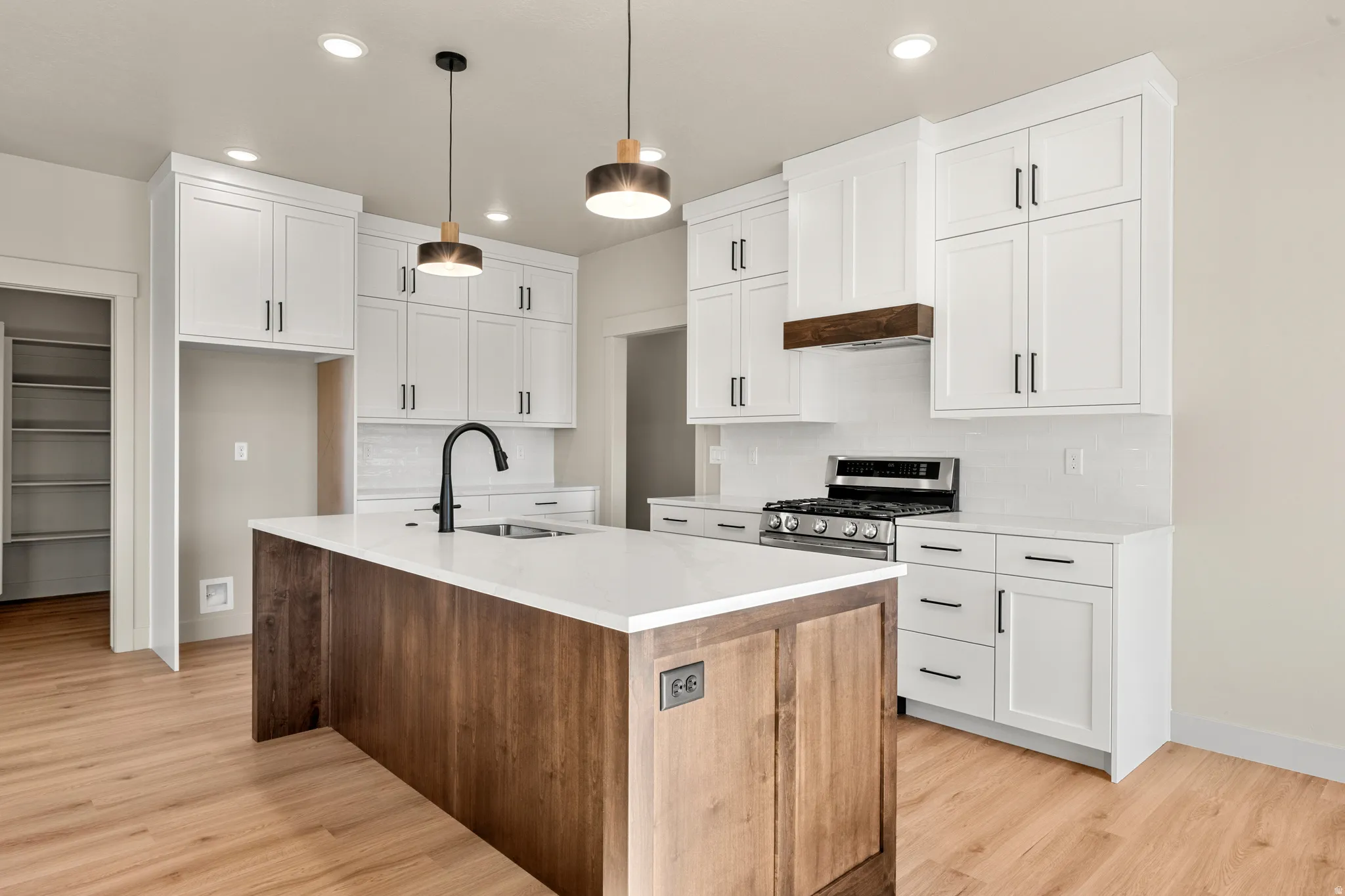 Kitchen with an island with sink, pendant lighting, decorative backsplash, white cabinetry, and light wood-type flooring