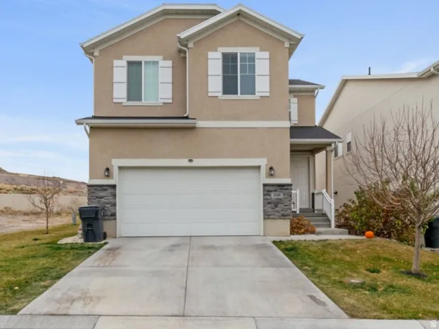 Traditional home with a front lawn, stucco siding, concrete driveway, stone siding, and a garage