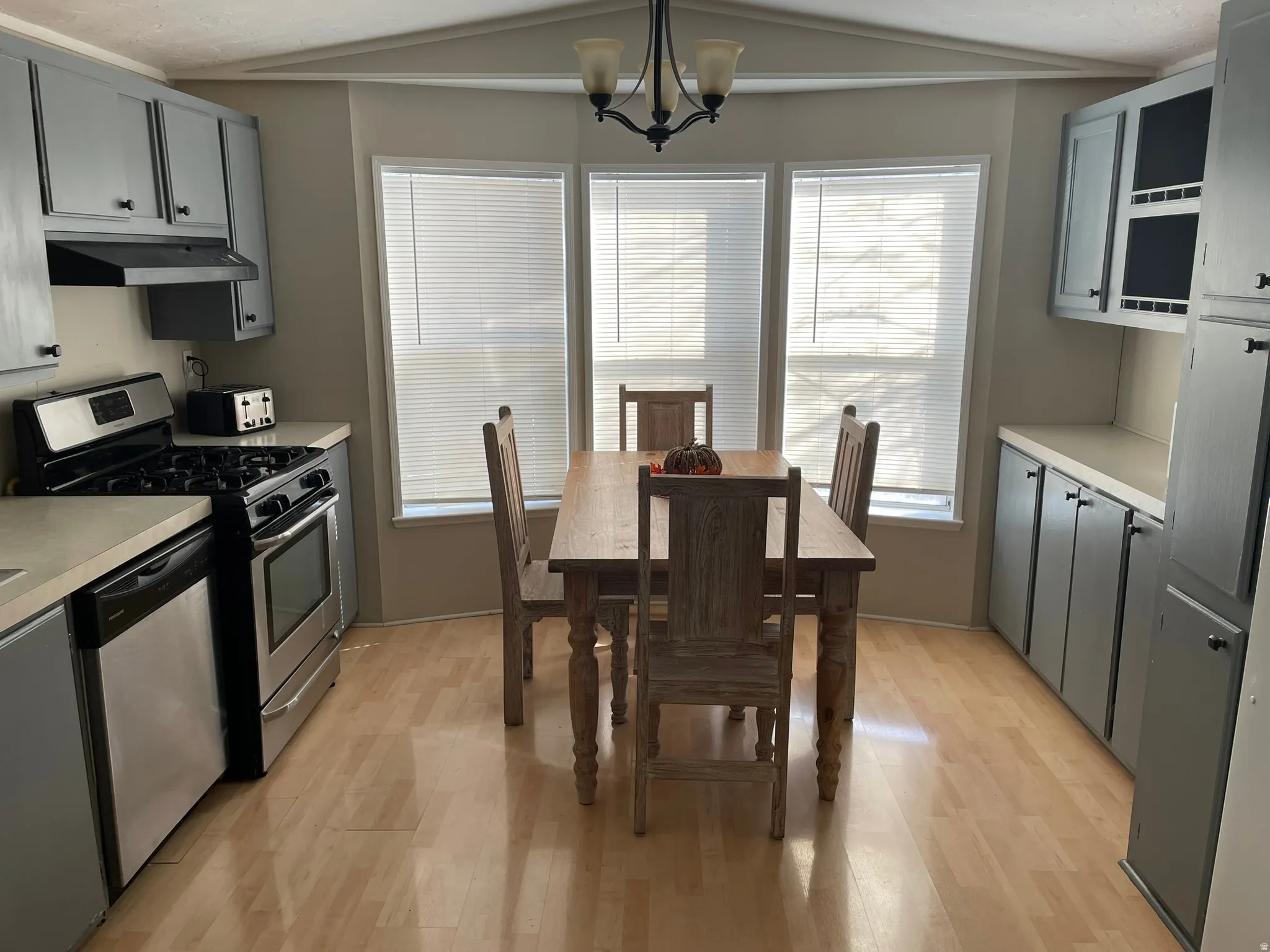 Kitchen with light countertops, appliances with stainless steel finishes, gray cabinets, vaulted ceiling, and light wood-type flooring