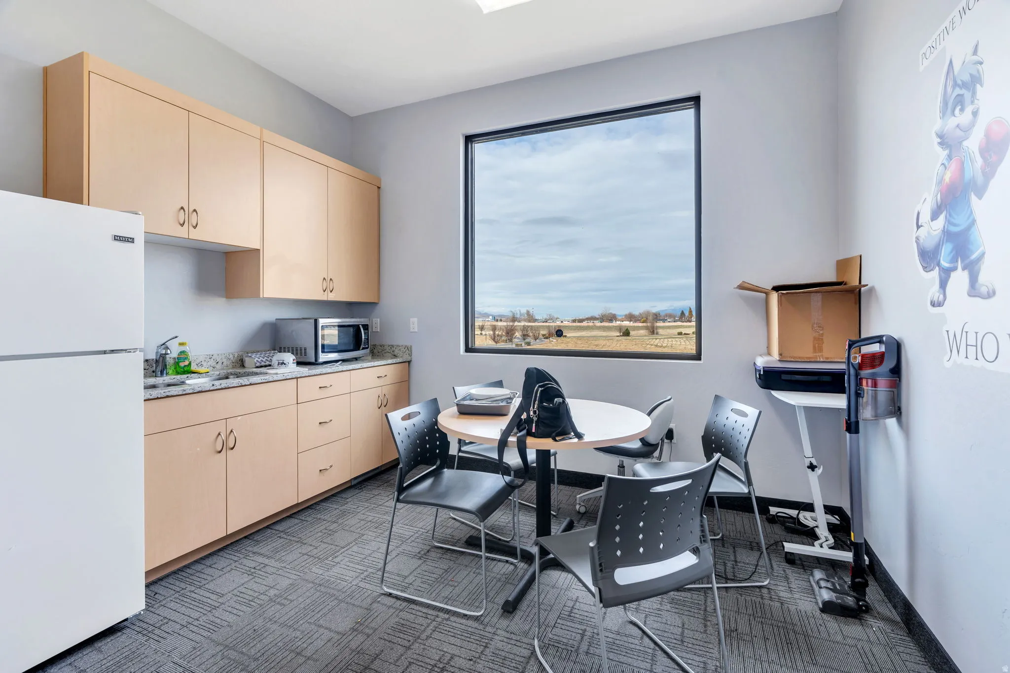 Kitchen featuring freestanding refrigerator, light brown cabinets, stainless steel microwave, and dark colored carpet